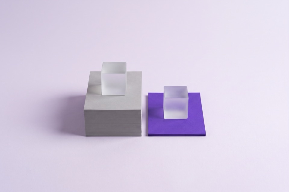 Two identical glass cubes, one on a tall grey stack and one on a thin violet slab