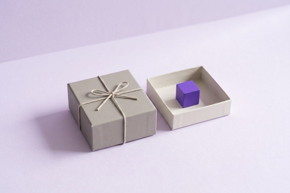 Grey box tied shut with string beside an open tray holding a violet cube