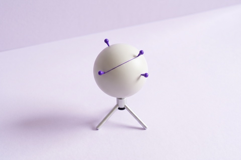 Small white globe on a tripod stand with violet pins joined by a violet thread